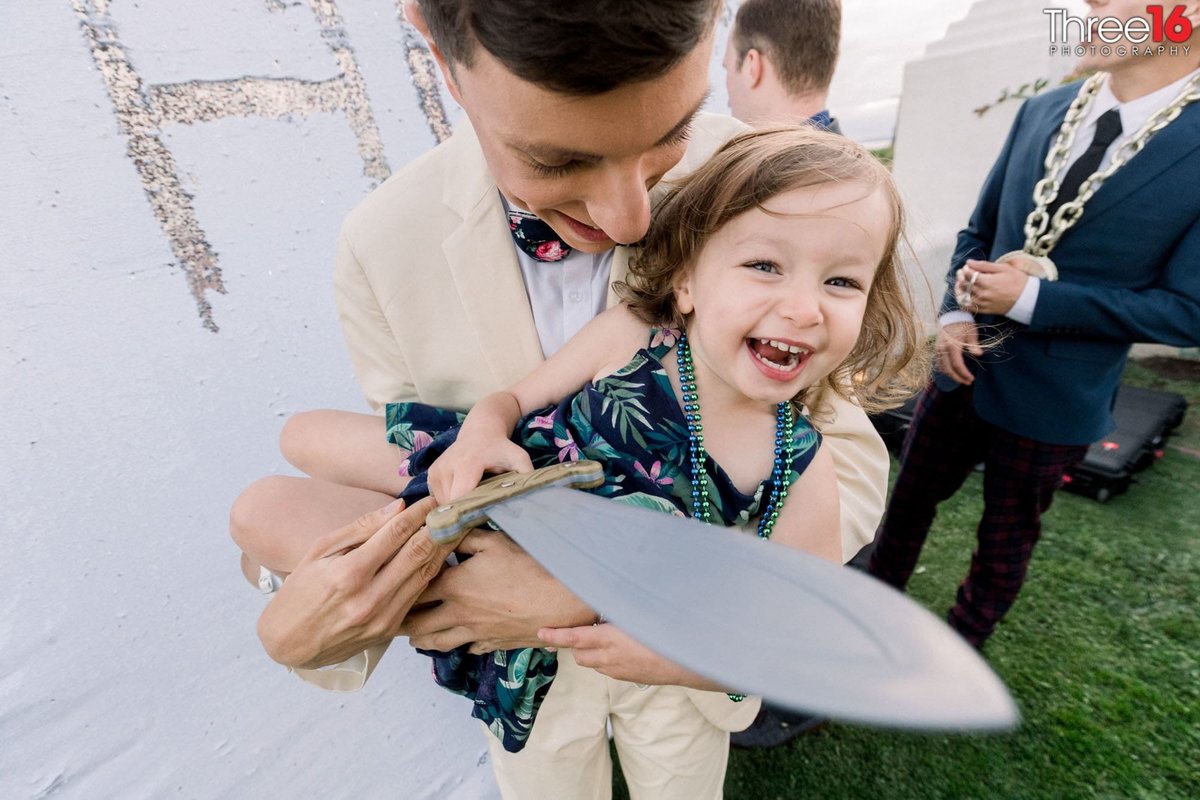 Little girl smiles as she is picked up and holding a plastic sword