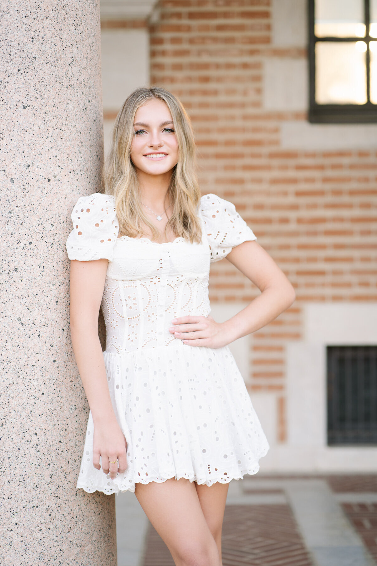 Picture of a teen senior in a white dress with her left arm on her hip.
