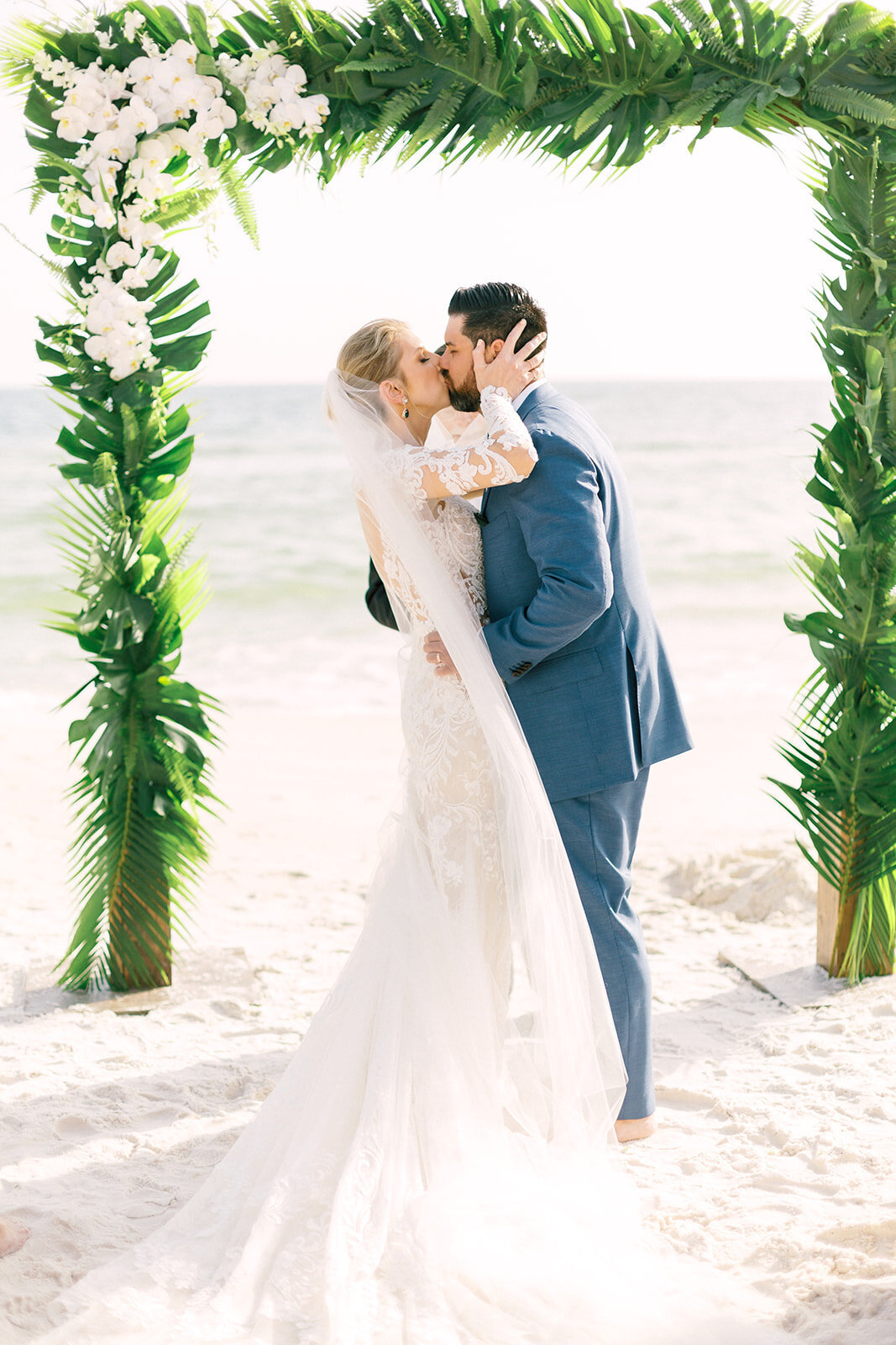 Bride and groom kiss after their vows in front of a tropical wedding altar on carillon beach
