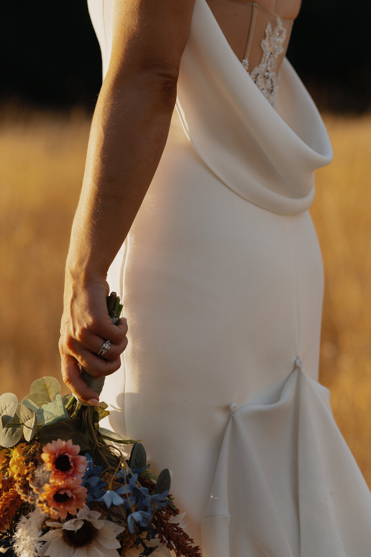 the back of a brides wedding dress and her bouquet at golden hour during her wedding portraits in Comox by Latitude 49 Photography