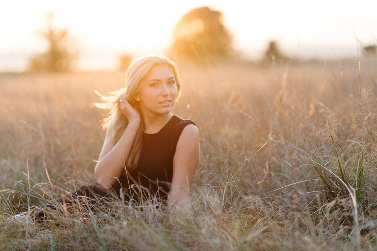 High school senior sitting in a grass field at sunset at Discovery Park.