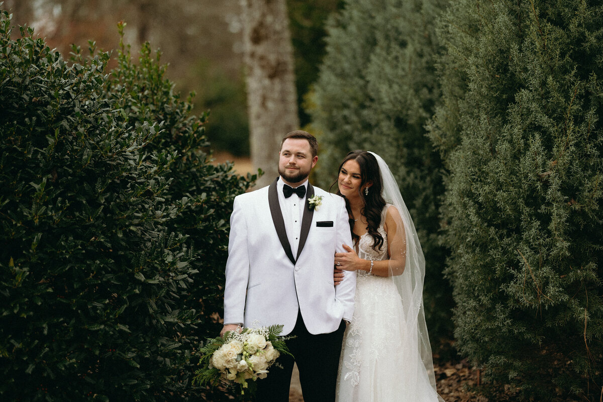 Couple standing amid lush green trees.