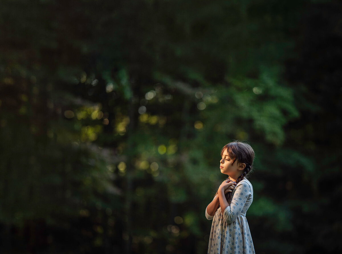 A young girl in a floral dress stands as the last sunlight of the day illuminates her face. 