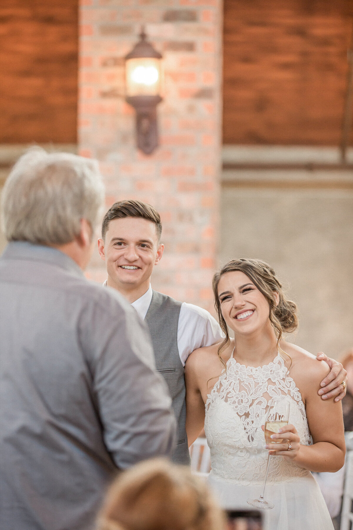 The bride and groom smile as they listen to her father give a toast during their reception.