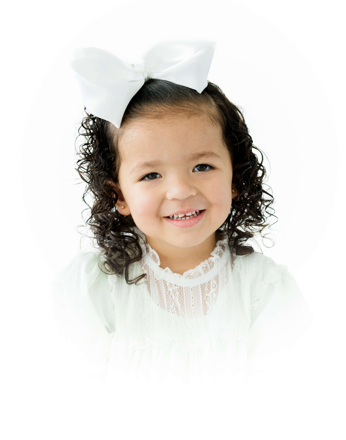 Girl with white bow in white heirloom outfit posing and smiling at the camera for heirloom photography session in Dothan Alabama