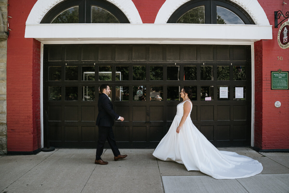 Groom walks towards bride in front of firehouse