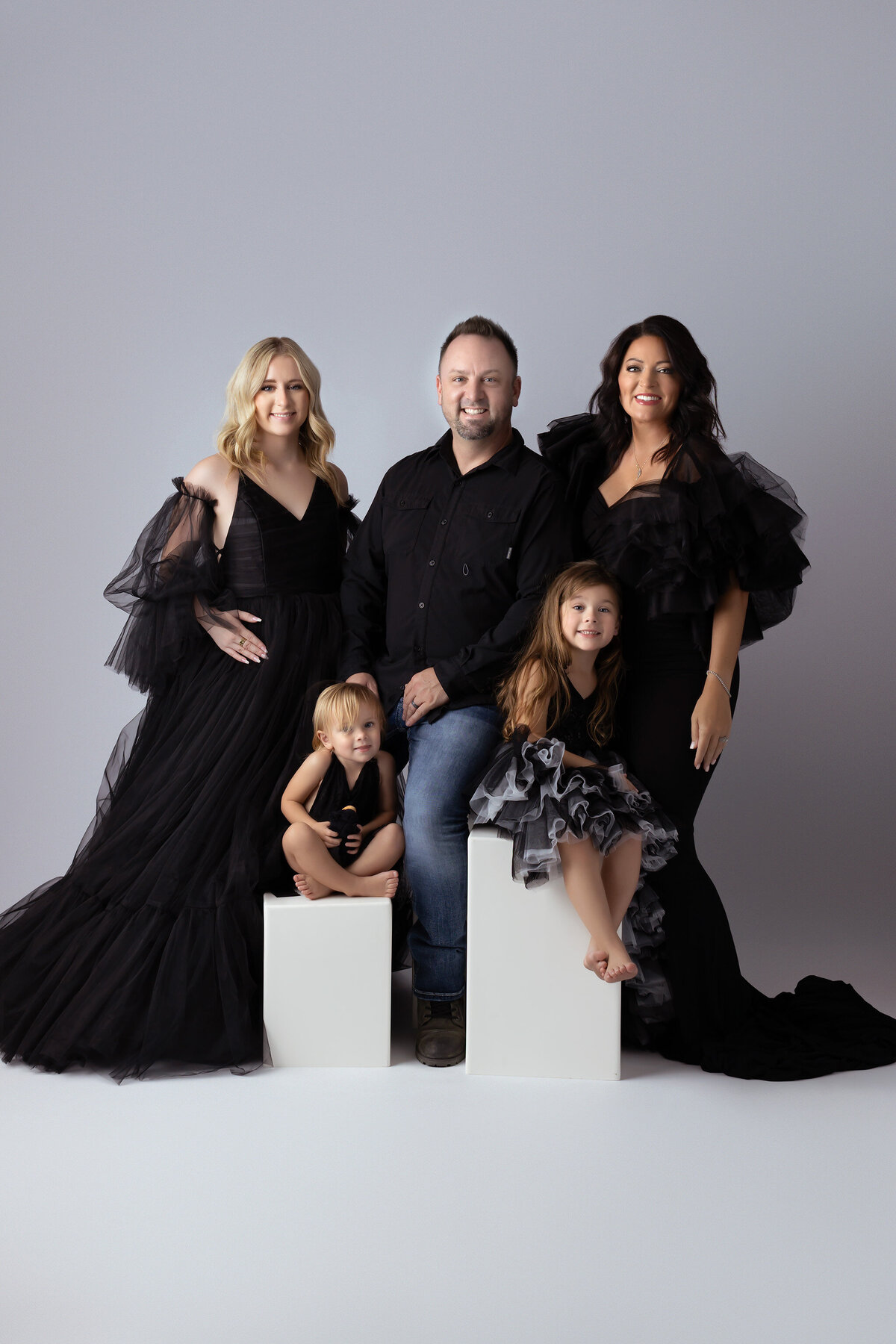 A stylish family portrait featuring a mother, father, two daughters, and a toddler in chic black gowns and clothing, created by a Dallas family photographer.