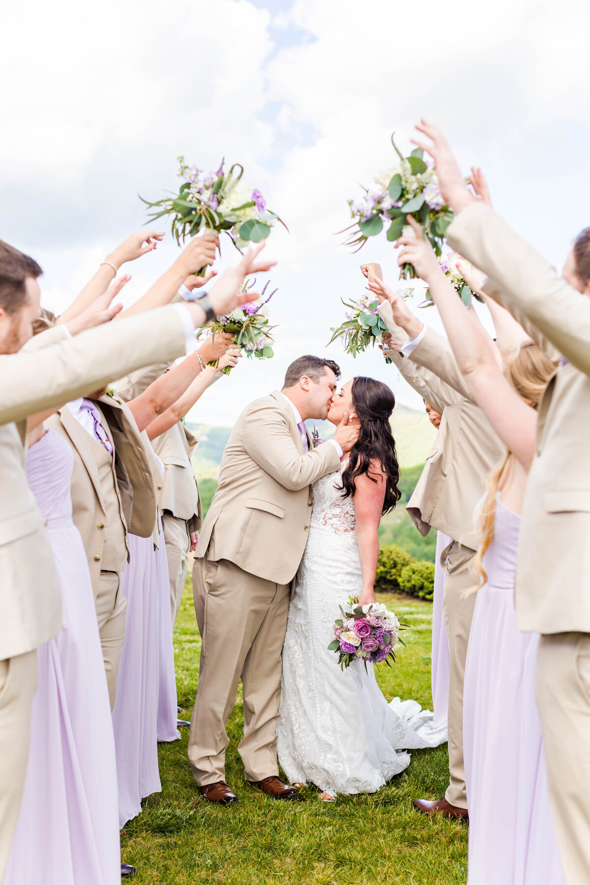 bride and groom kissing with wedding party holding their bouquets in air
