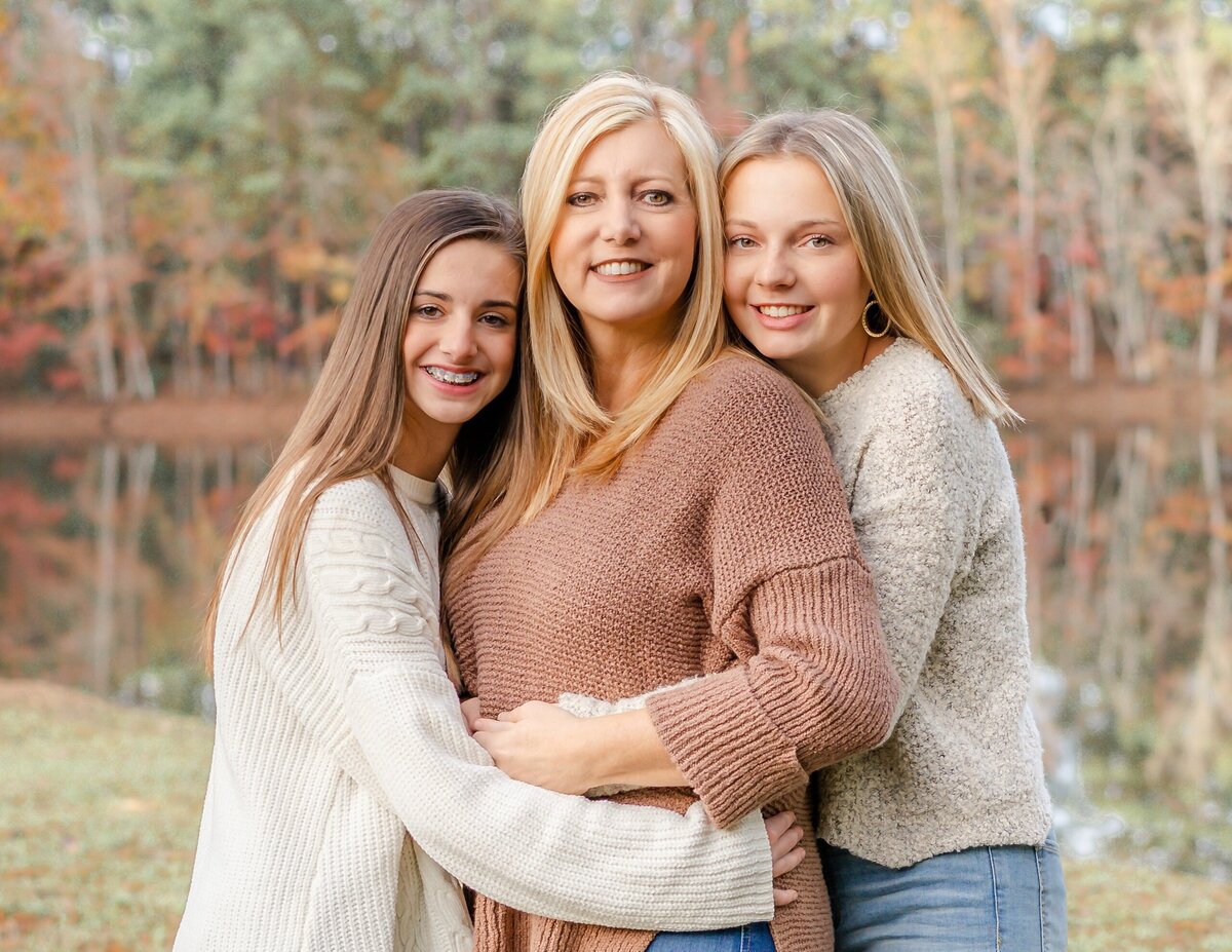 two daughters hugging their mom on a pond in their backyard during this autumn photo shoot