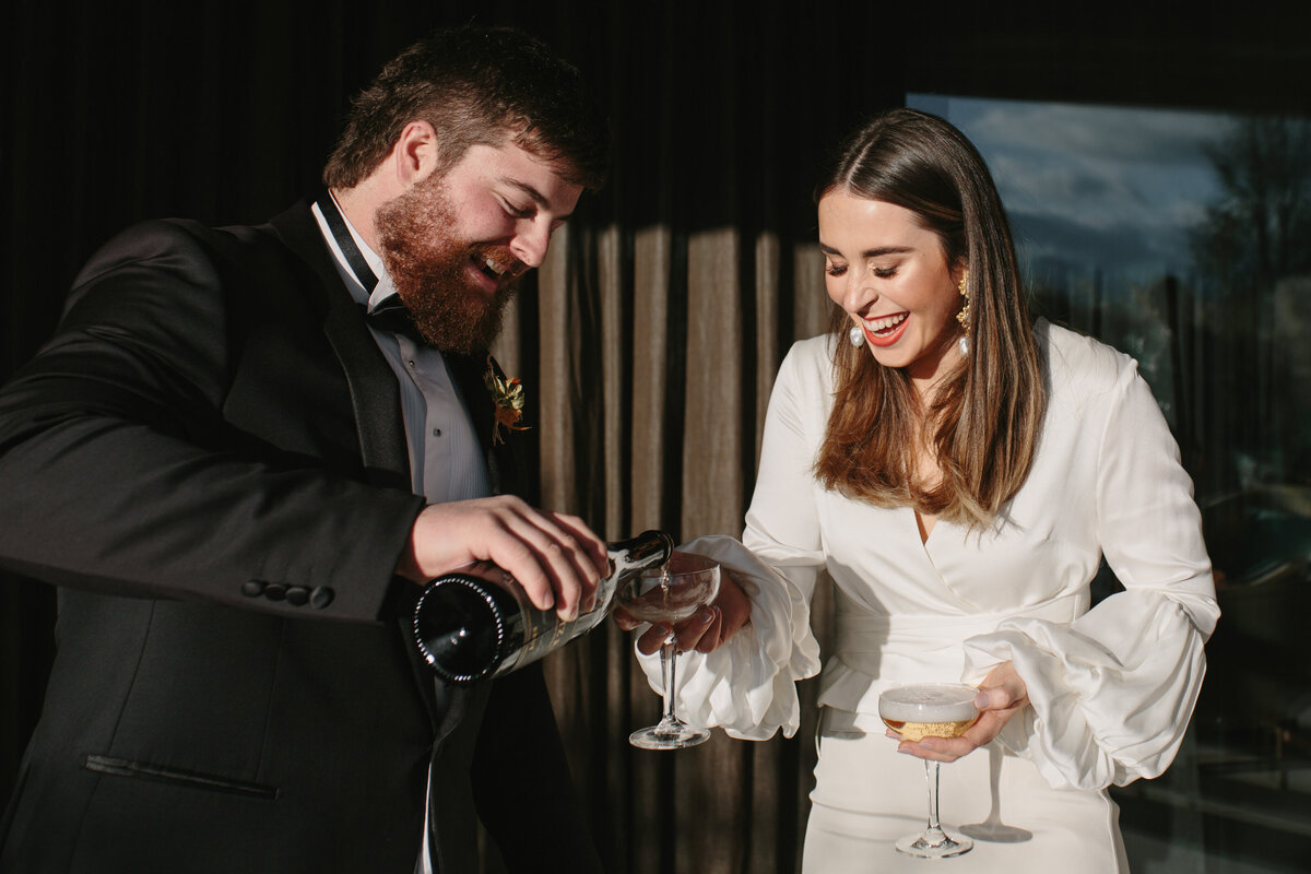 The Lovers Elopement Co - groom pours bride champagne after wedding ceremony