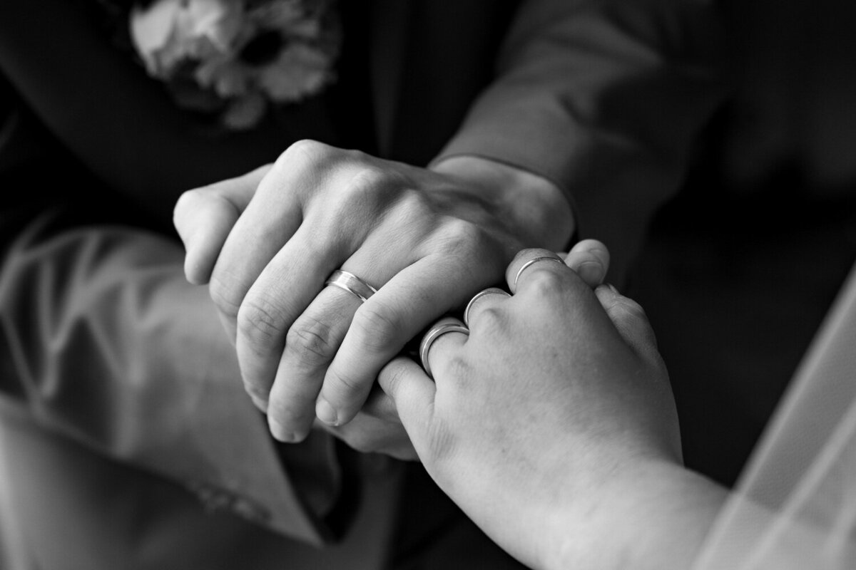 black and white closeup image of two hands adorned with wedding bands