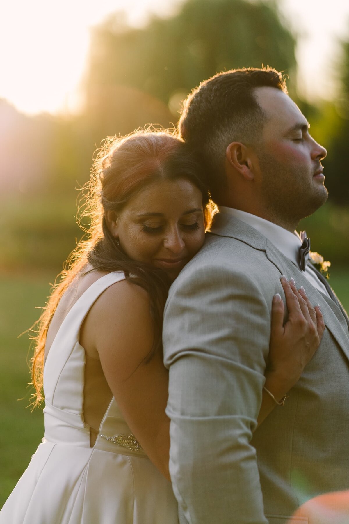 bride hugging groom from behind as the sunsets