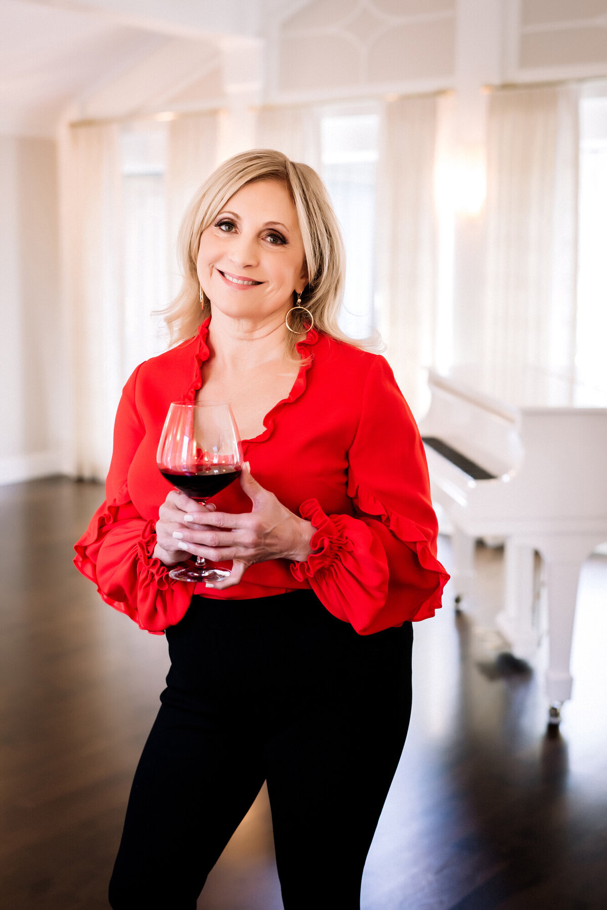 A female dating portrait client. wearing a red blouse, holding a glass of red wine in her living room