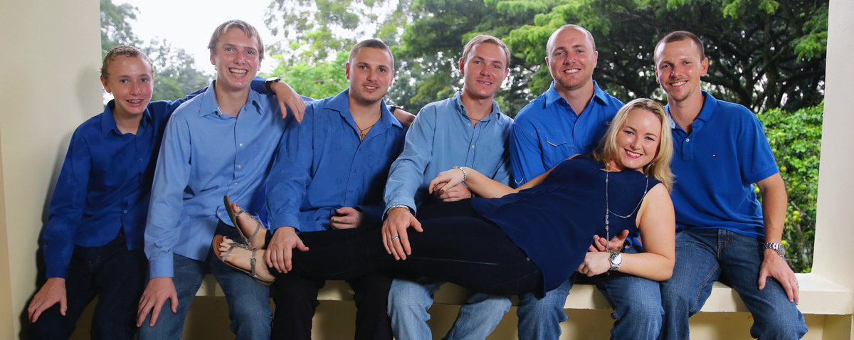Portrait of family dressed in blue with mom lying across all their laps. Photo by Ross Photography, Trinidad, W.I..