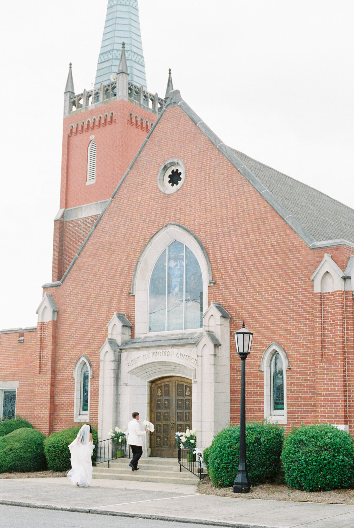 A bride and groom walk into a church with a large steeple by Huntsville wedding photographer, Kelsey Dawn Photography