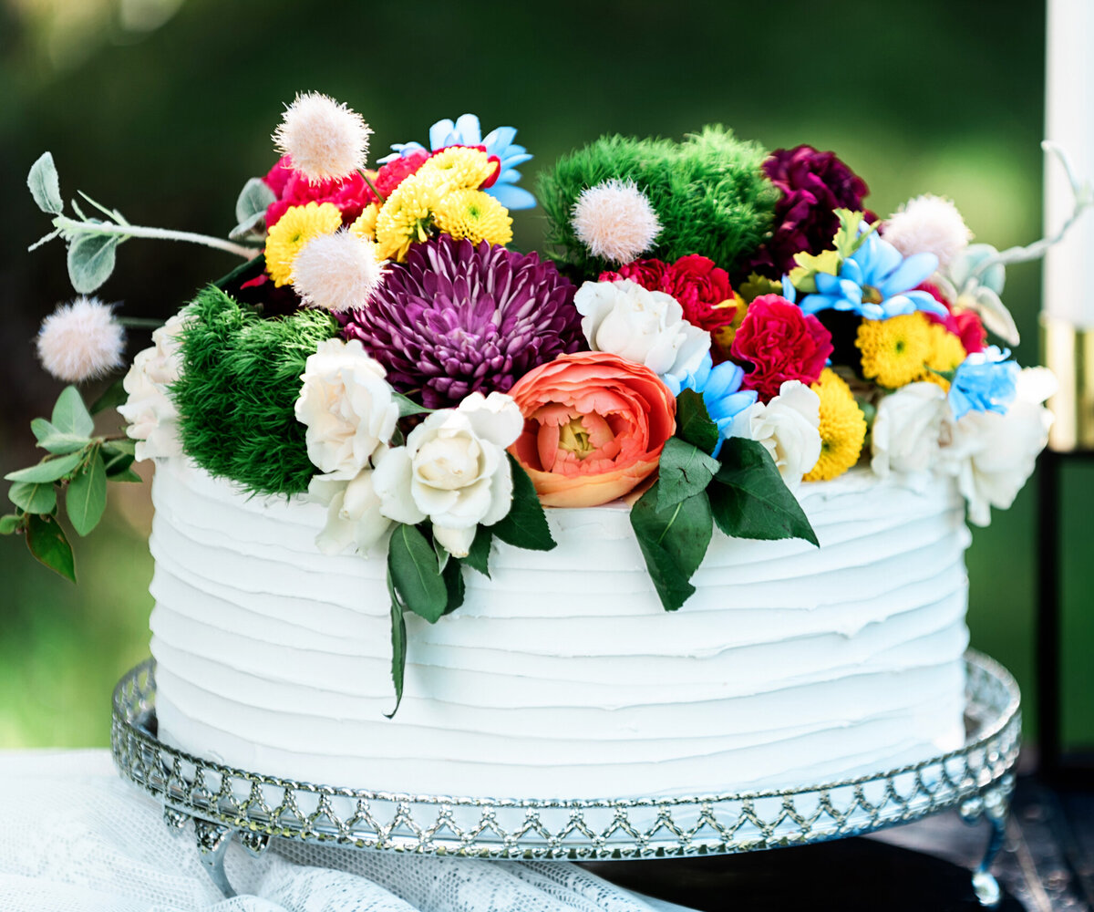 Professional custom single-tiered white wedding cake, topped with colourful Spring florals, created by Black Dog Bakery, creative & eclectic cakes & desserts in Calgary, Alberta, featured on the Brontë Bride Vendor Guide.