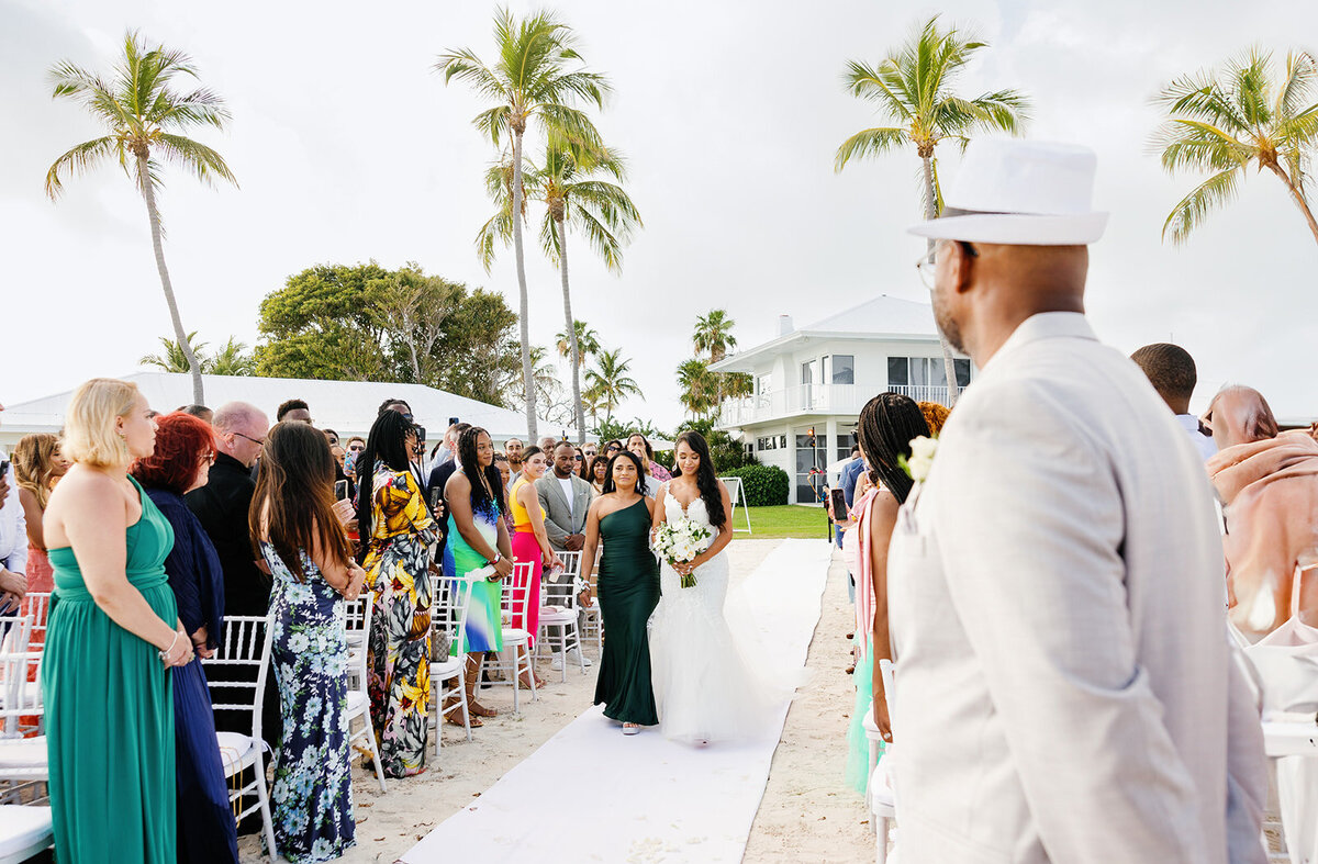 Jonathan stands at the altar, looking towards his bride Andressa as she walks down the white aisle at their seaside wedding in Table Key, Islamorada. Photography by Claudia Amalia.