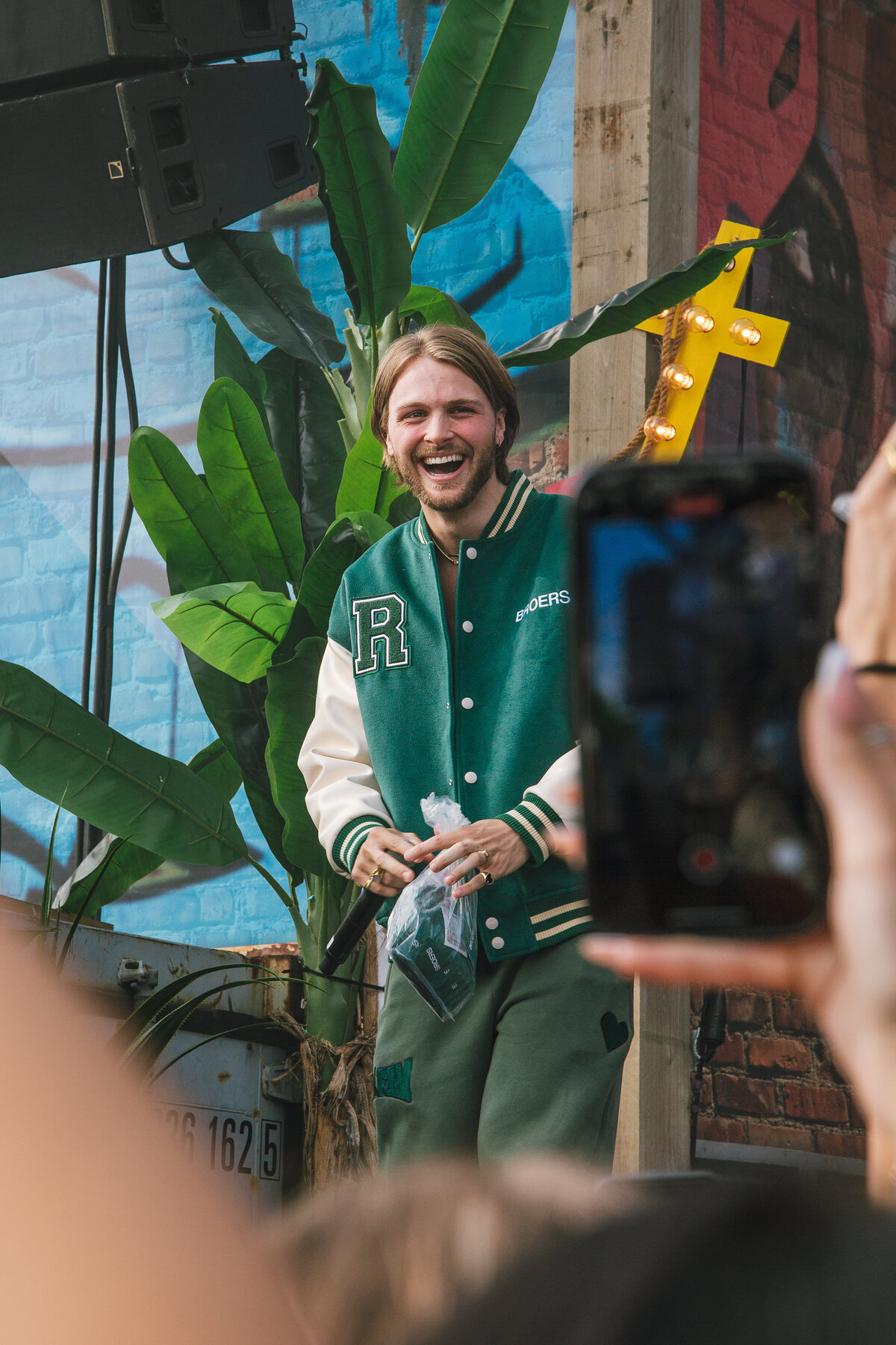 Sam Hofman is captured in a candid moment, deeply focused while holding a microphone and a drink. The image highlights his thoughtful expression amidst the backstage environment. Photographed by Bo Eppink.