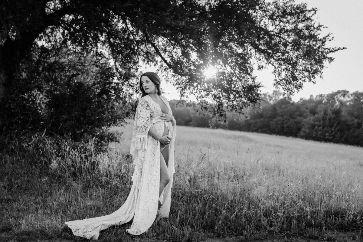 Black and white maternity photo in Dallas,TX. A woman standing in a meadow. She is looking back at a tree.