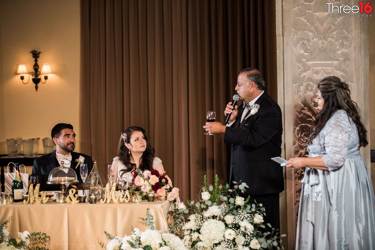 Bride and Groom sit at the sweetheart table as the Bride's parents toast them