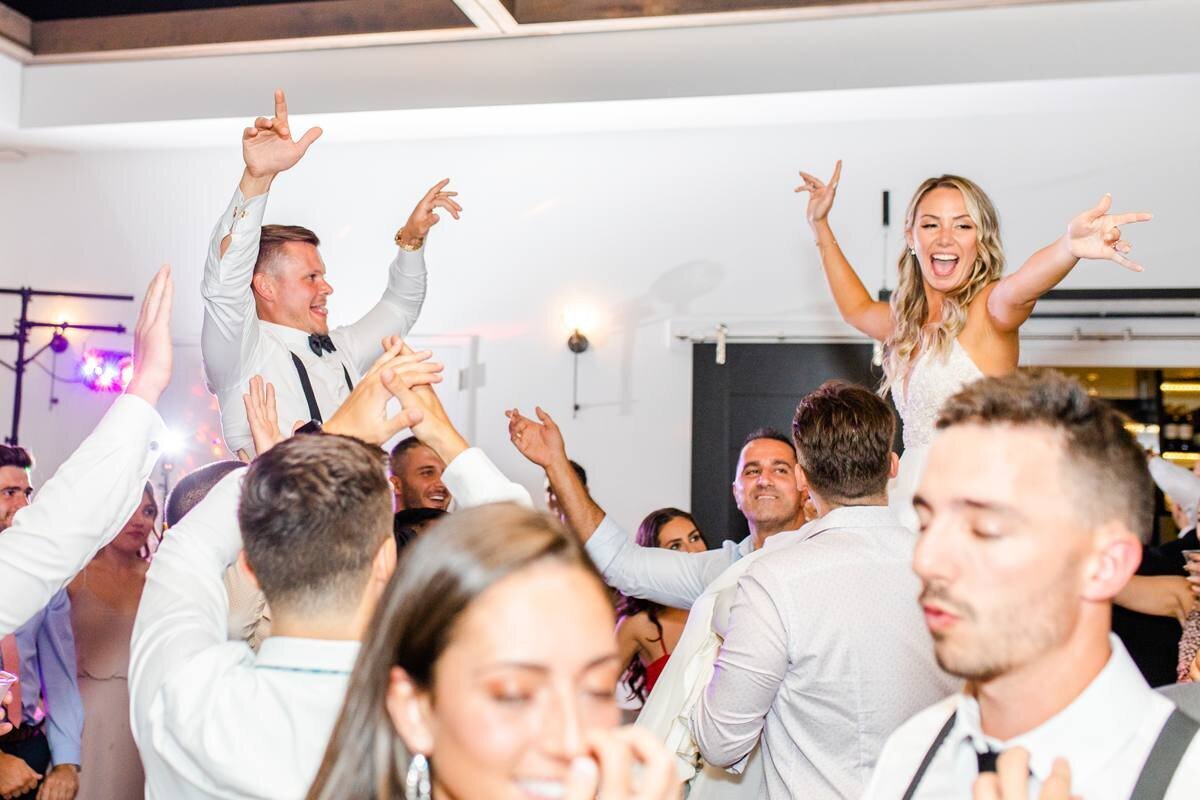bride and groom get lifted onto shoulders of wedding guests during reception dancing