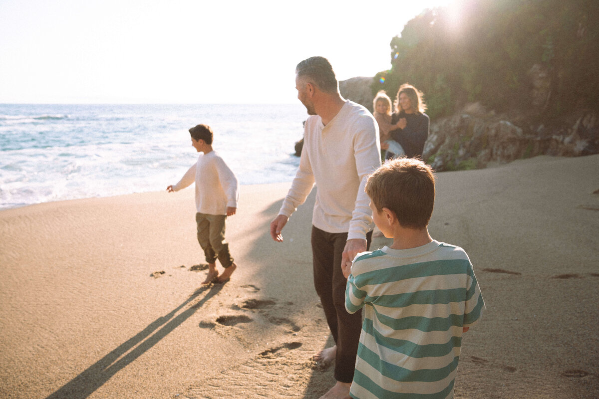 Candid family photo at Laguna Beach with parents and kids running from ocean wave during Southern California photo session