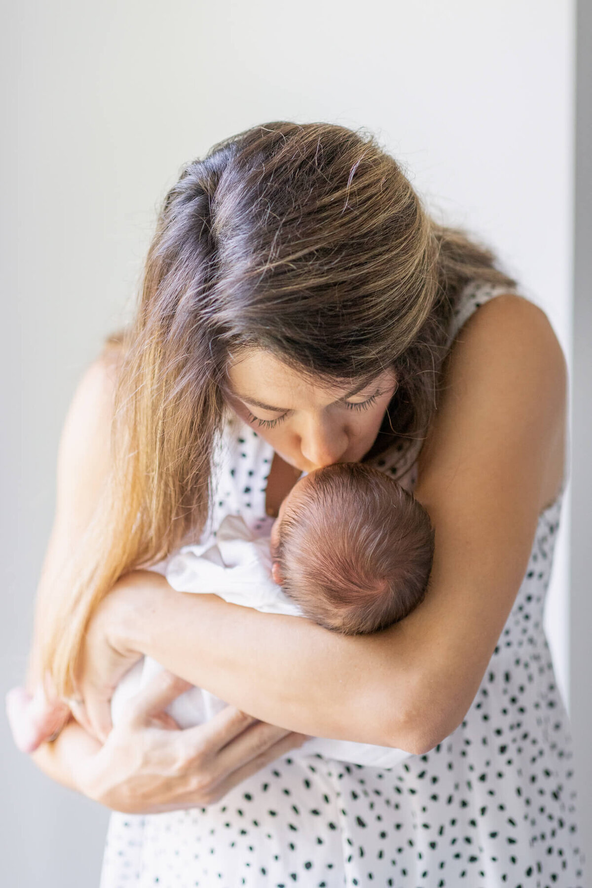 Mom in a polka dot dress holding and kissing her newborn baby