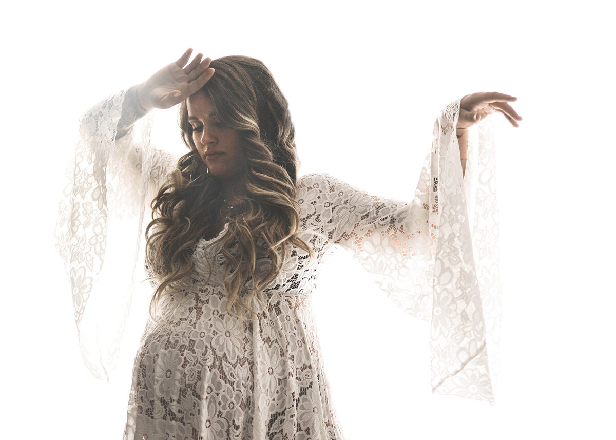 An Iowa maternity photography session image of a pregnant woman dancing in a studio in a lace maternity gown