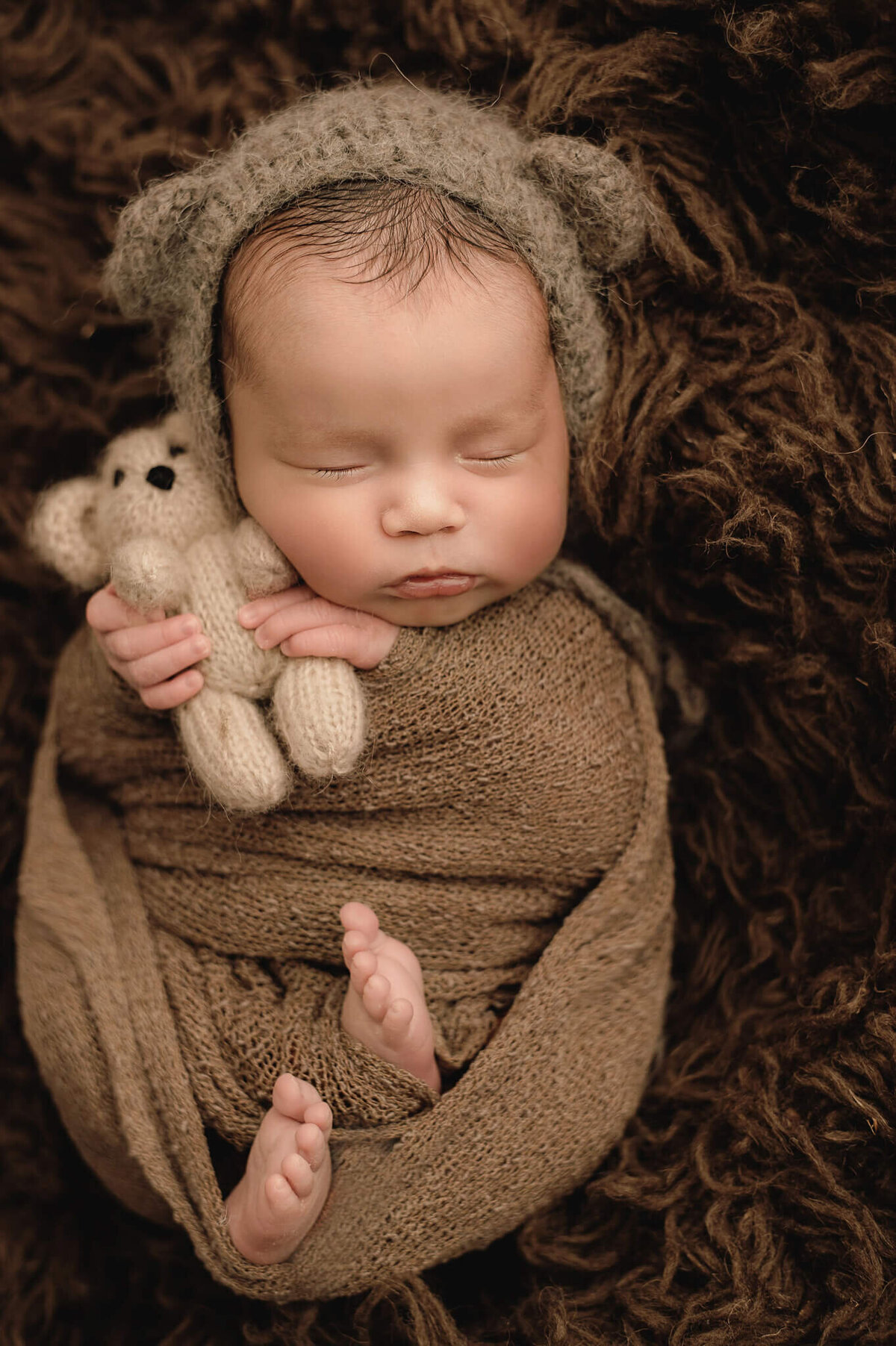 Greater Toronto Newborn photo of baby boy wearing a bear hat holding a little teddy.