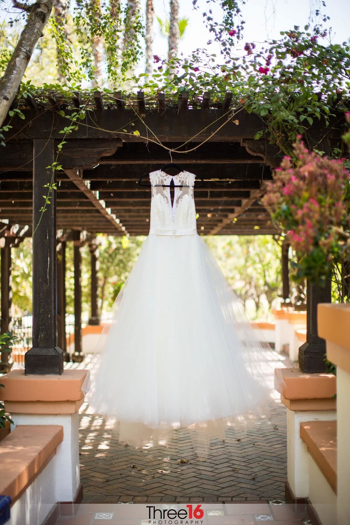 Beautiful Bridal Gown hangs on display off a patio trellis