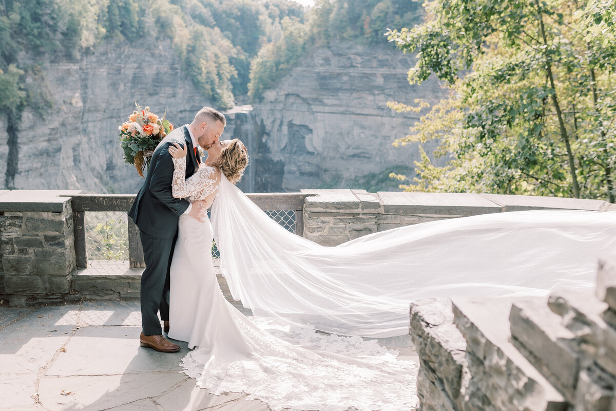 A bride and groom kissing during their elopement at the overlook at Taughannock State park with the waterfall behind them.