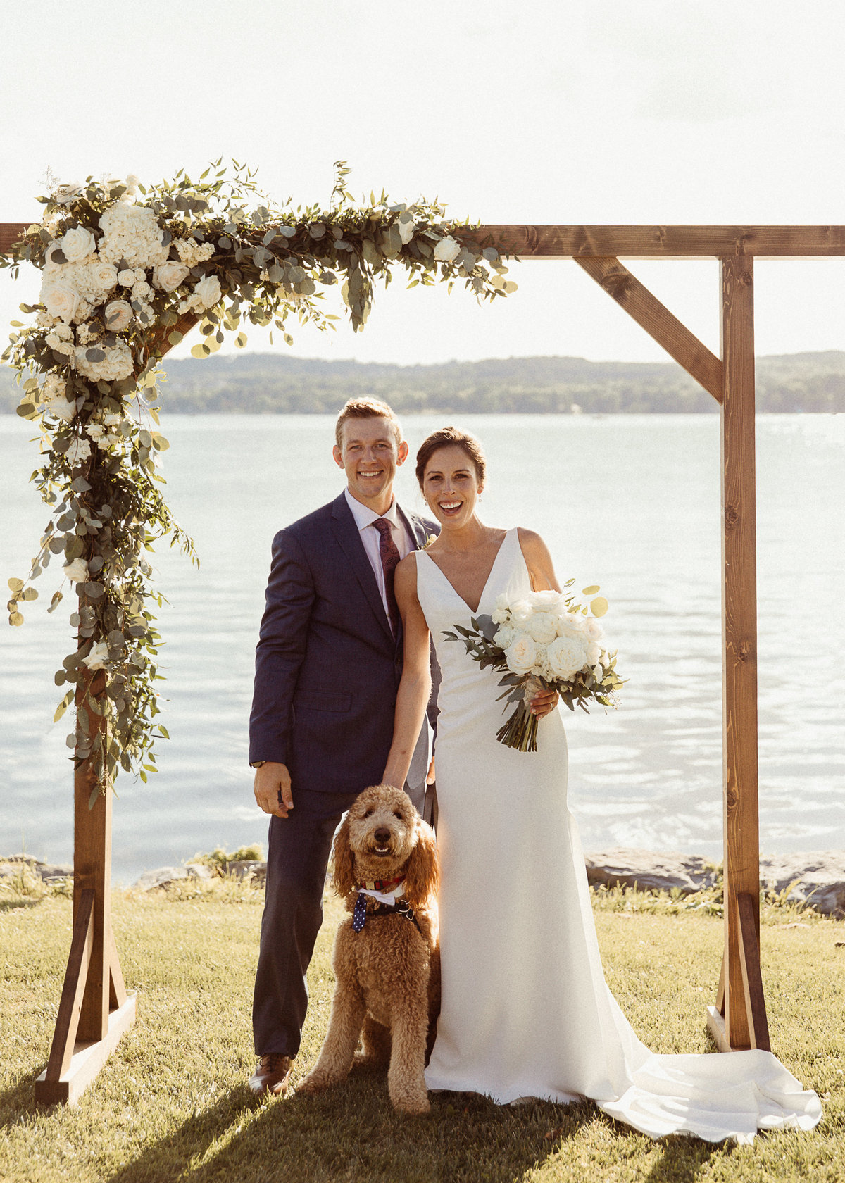 bride and groom under a wedding arch with their dog