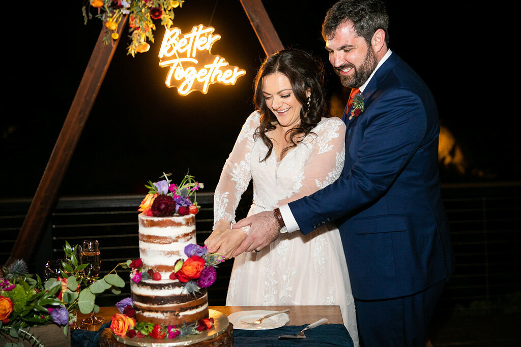 Bride and groom cut their cake in front of a neon sign