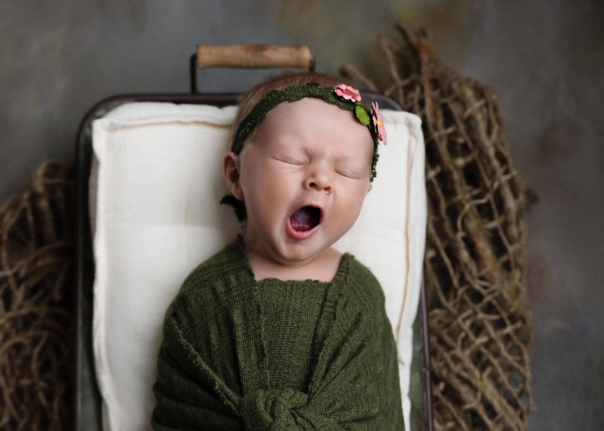 newborn baby yawning laying in a prop bowl