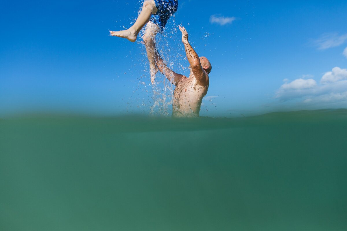 dad throwing son in the air from the water