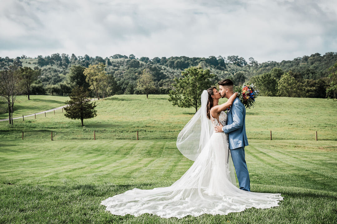 Bride and groom share a romantic kiss during an outdoor wedding ceremony on a scenic estate in New Jersey, with rolling hills in the background.