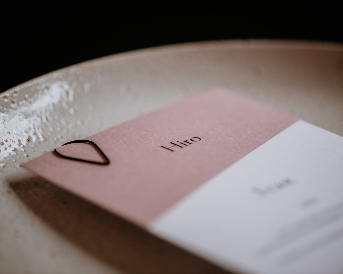 Pink place card layered with white wedding reception menu and black teardrop clasp