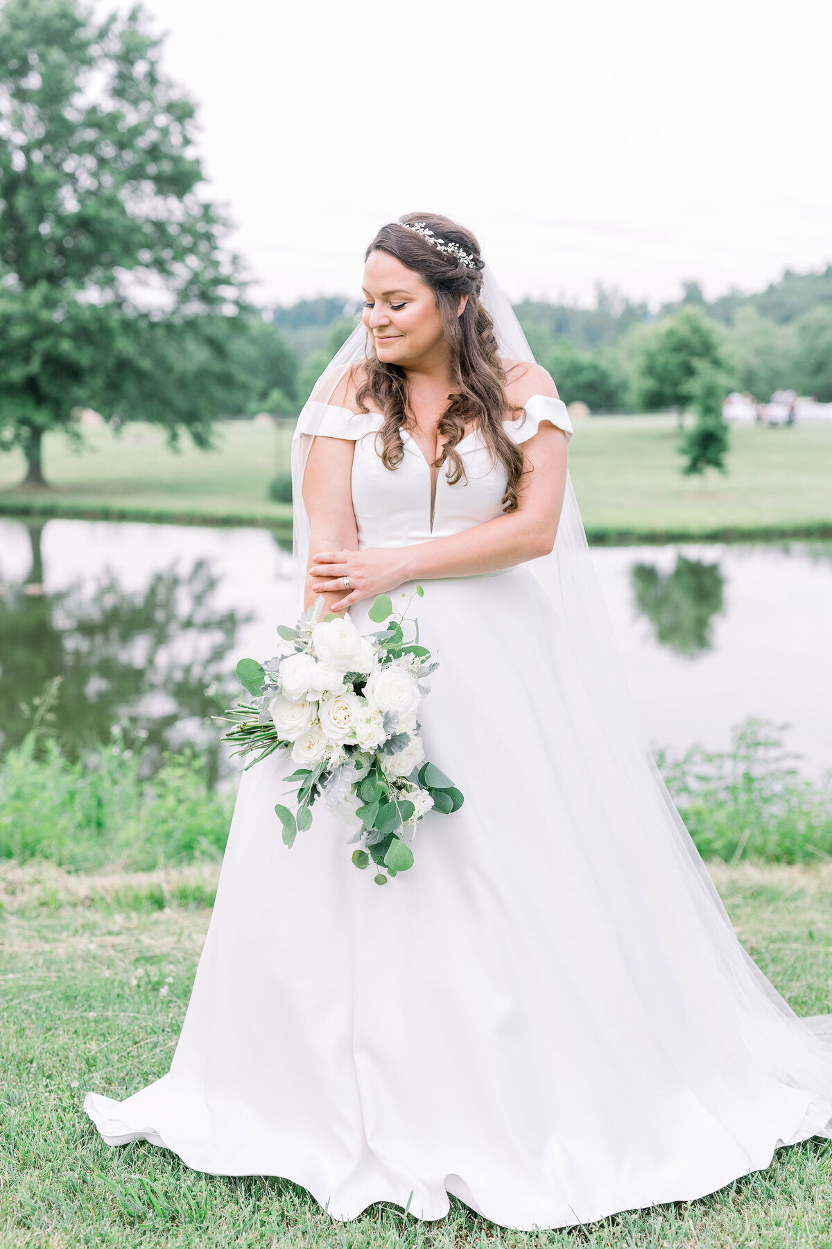 bride with off the shoulder deep V wedding dress in front of pond