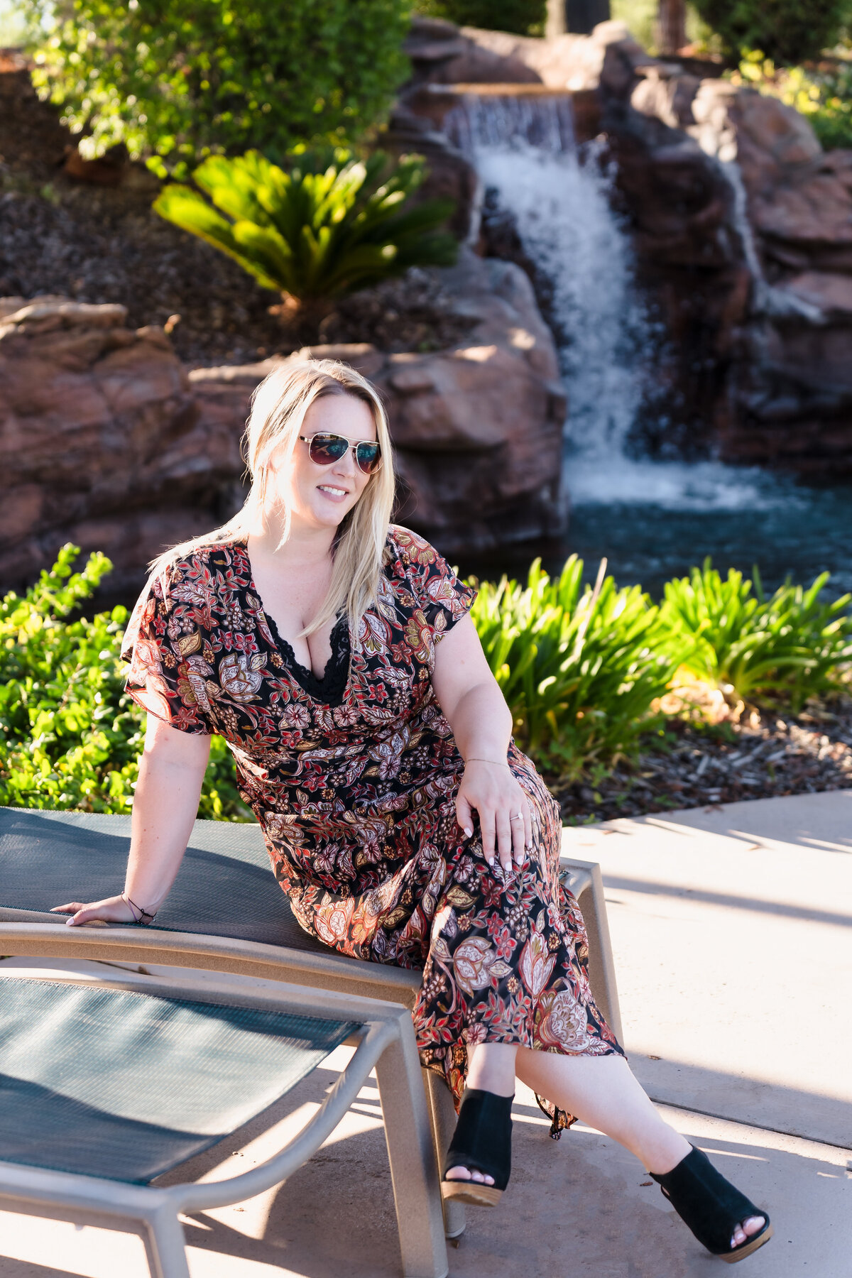 brand photo of a life coach  posing outside, in a pool area, legs crosses , wearing high heels