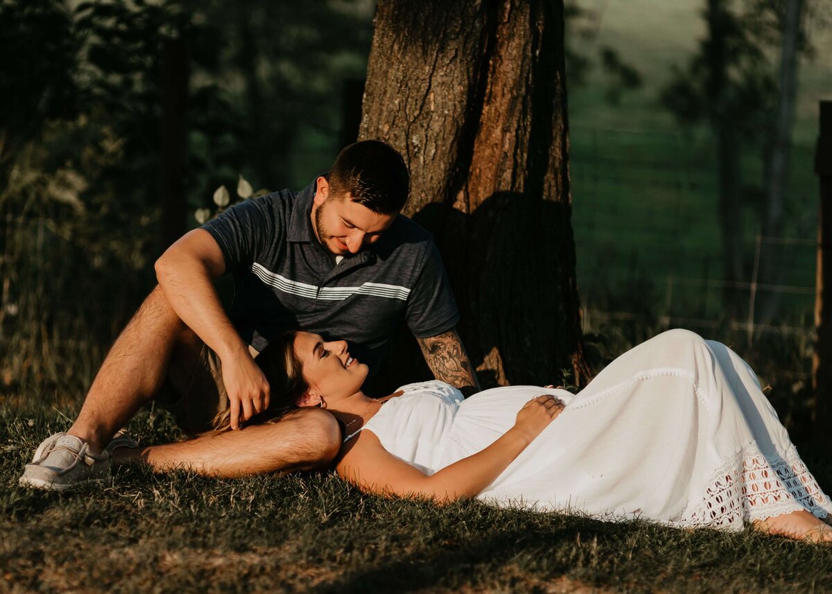 A couple laying on the grass next to a tree.