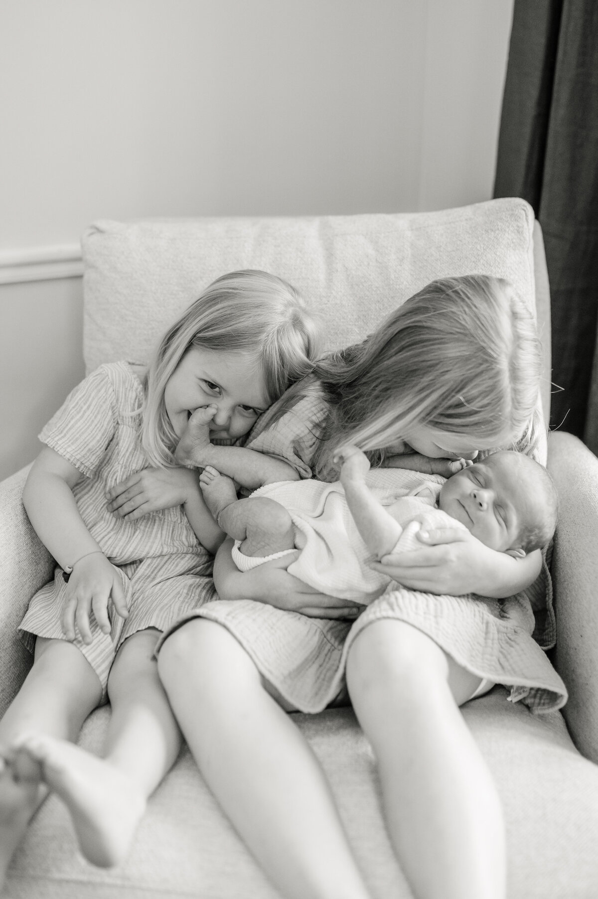 Two girls ages 5 and 7 are sitting in a rocker chair holding their newborn baby brother during a Milwaukee photo session