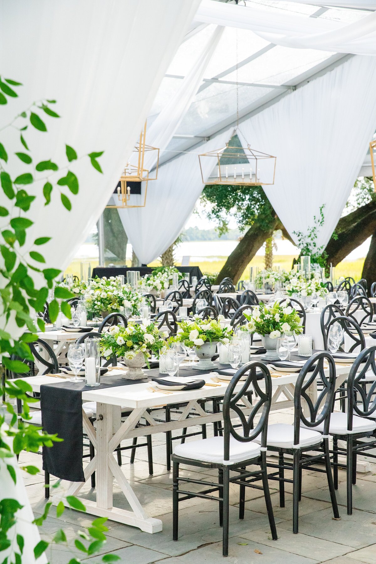 white farm tables with black chairs with greenery at lowndes grove charleston sc