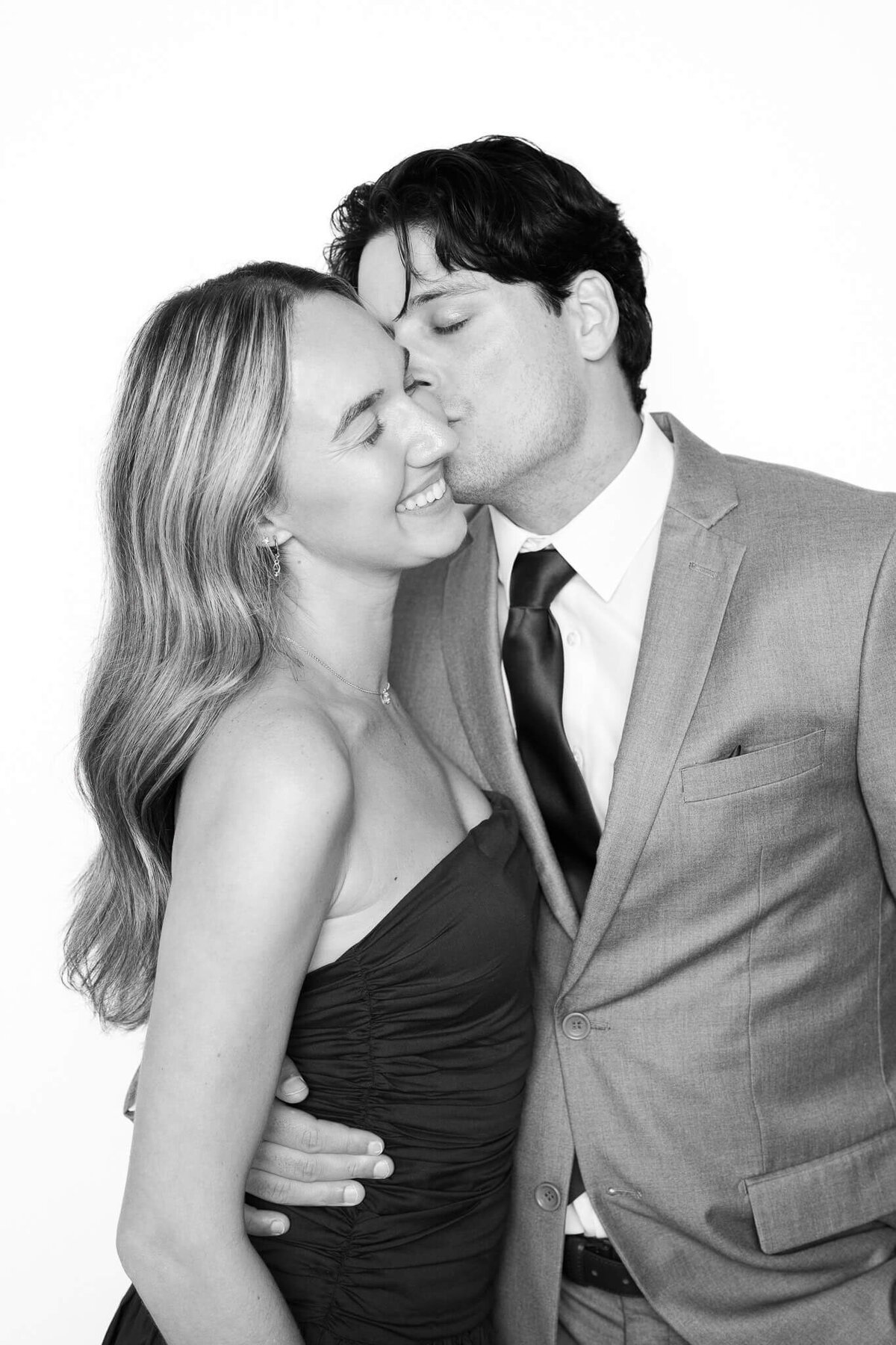 A joyful couple shares a sweet kiss in a classic black and white portrait by Monochrome Portraits, a Phoenix photo booth rental creating refined event photography.