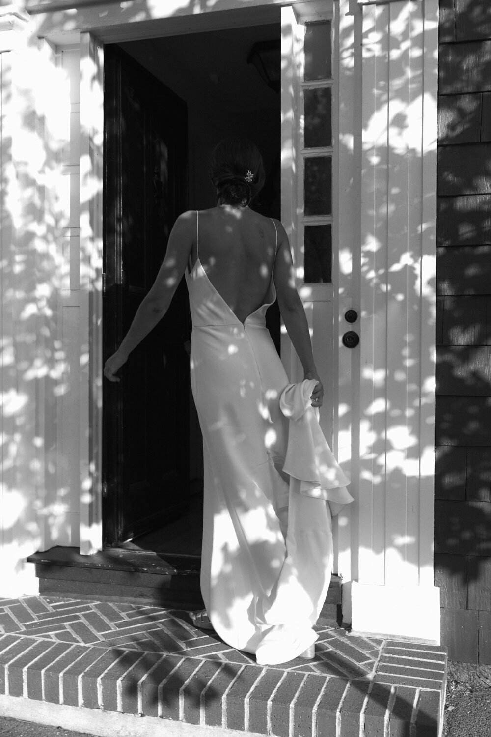 Bride entering a doorway, captured in black and white, with sunlight casting shadows