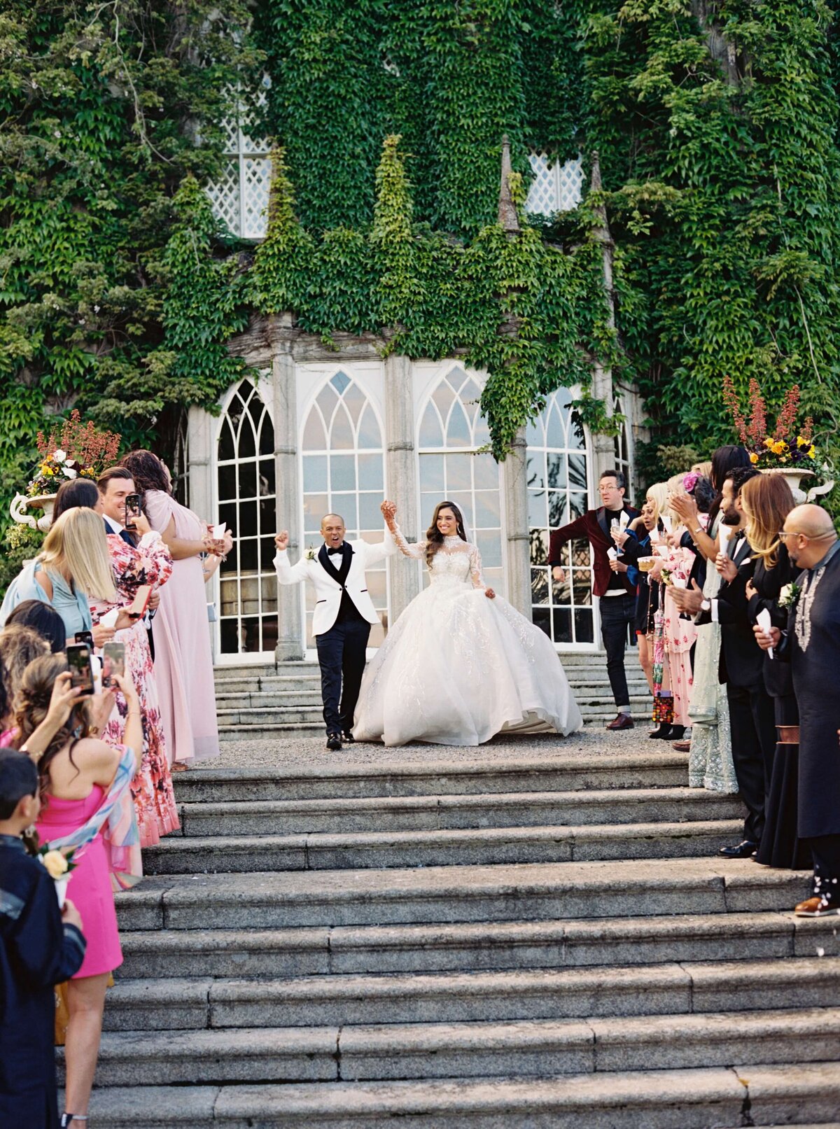 A wedding photo of the married couple holding hands and celebrating with their friends at Luttrellstown Castle in Ireland