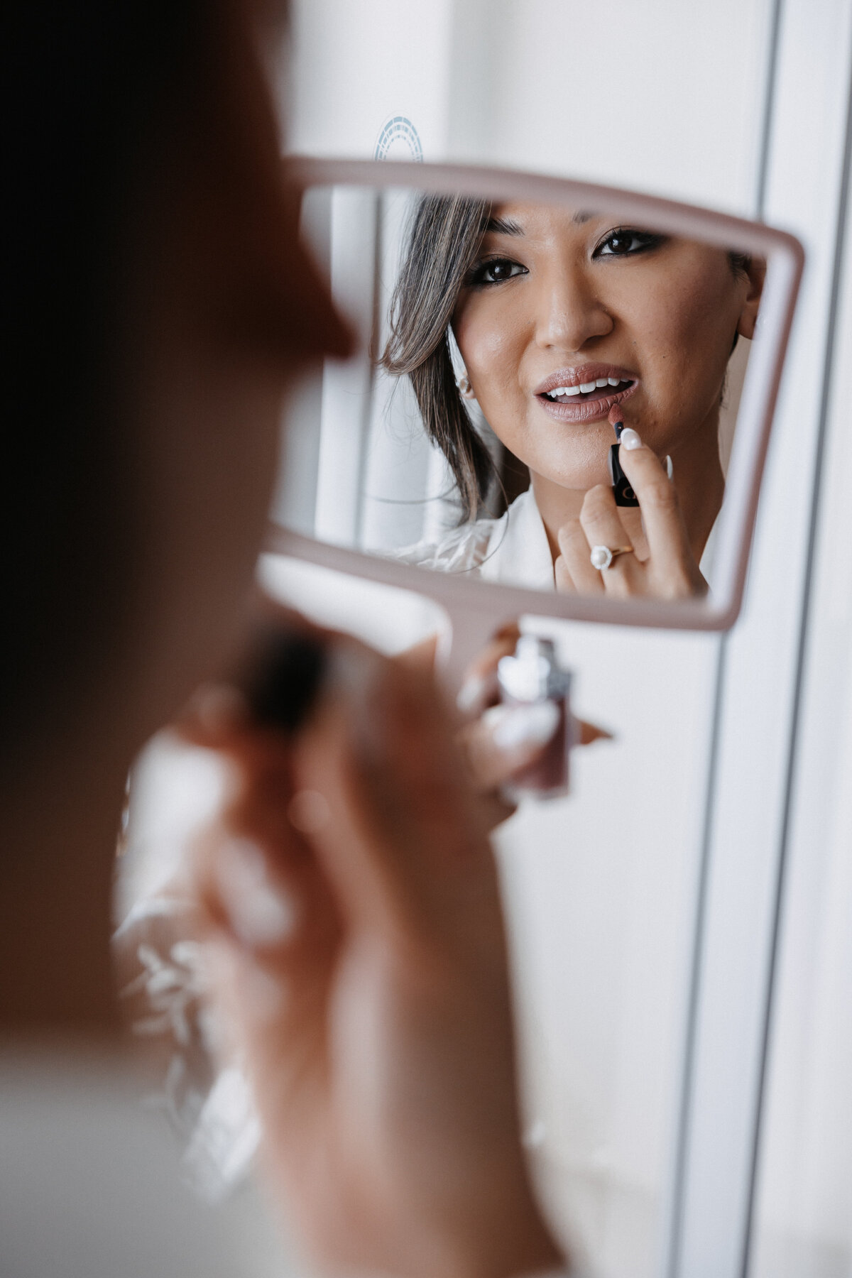 Bride in lace robe applying lipgloss in a mirror