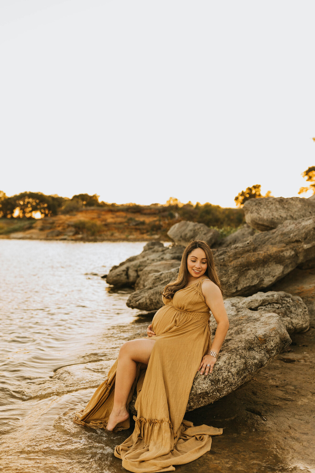 Pregnant mother in a dramatic mustard linen dress sitting on a boulder at Lake Grapevine