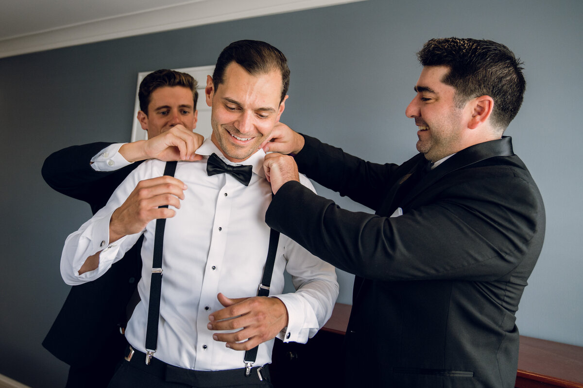 A group of groomsmen helping each other with their suspenders.