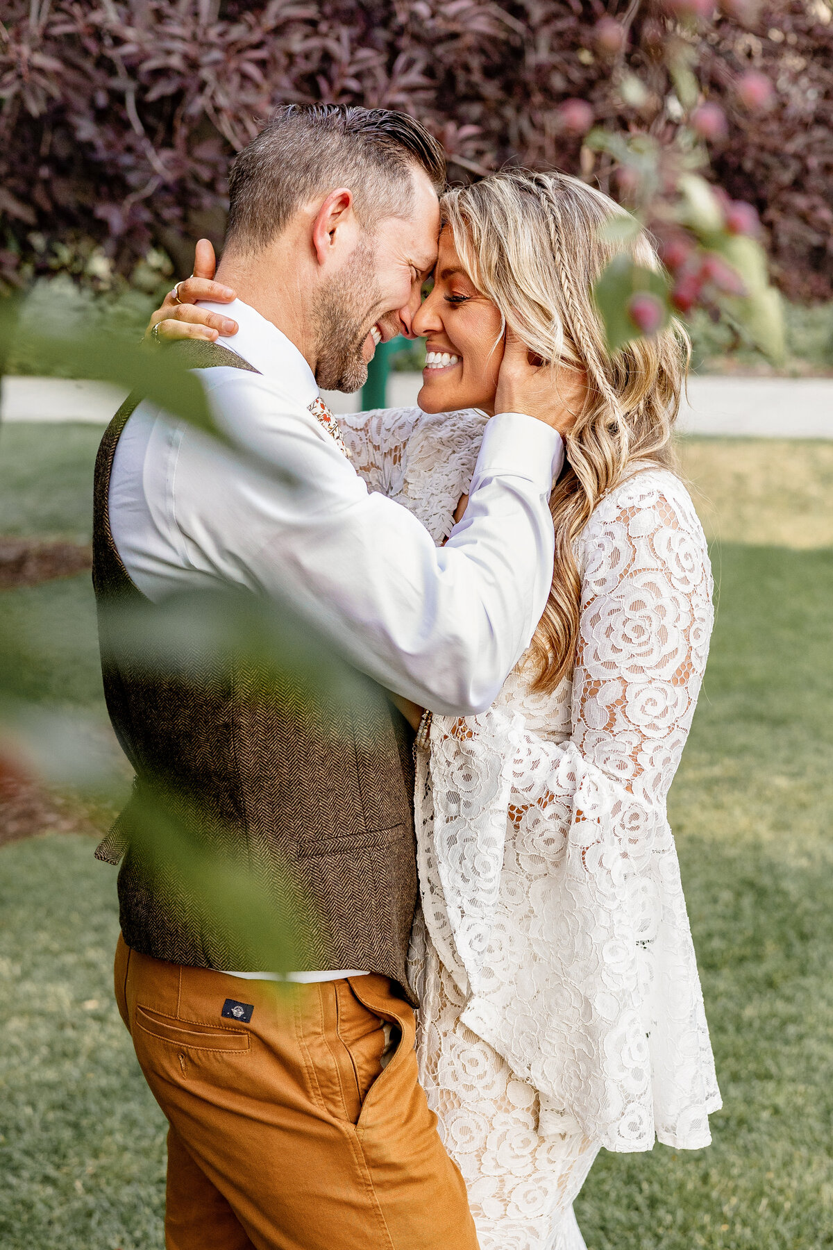 The bride and groom embrace with foreheads touching, smiling with closed eyes and soaking in a quiet, joyful moment after their ceremony in the Provo Canyon greenery.