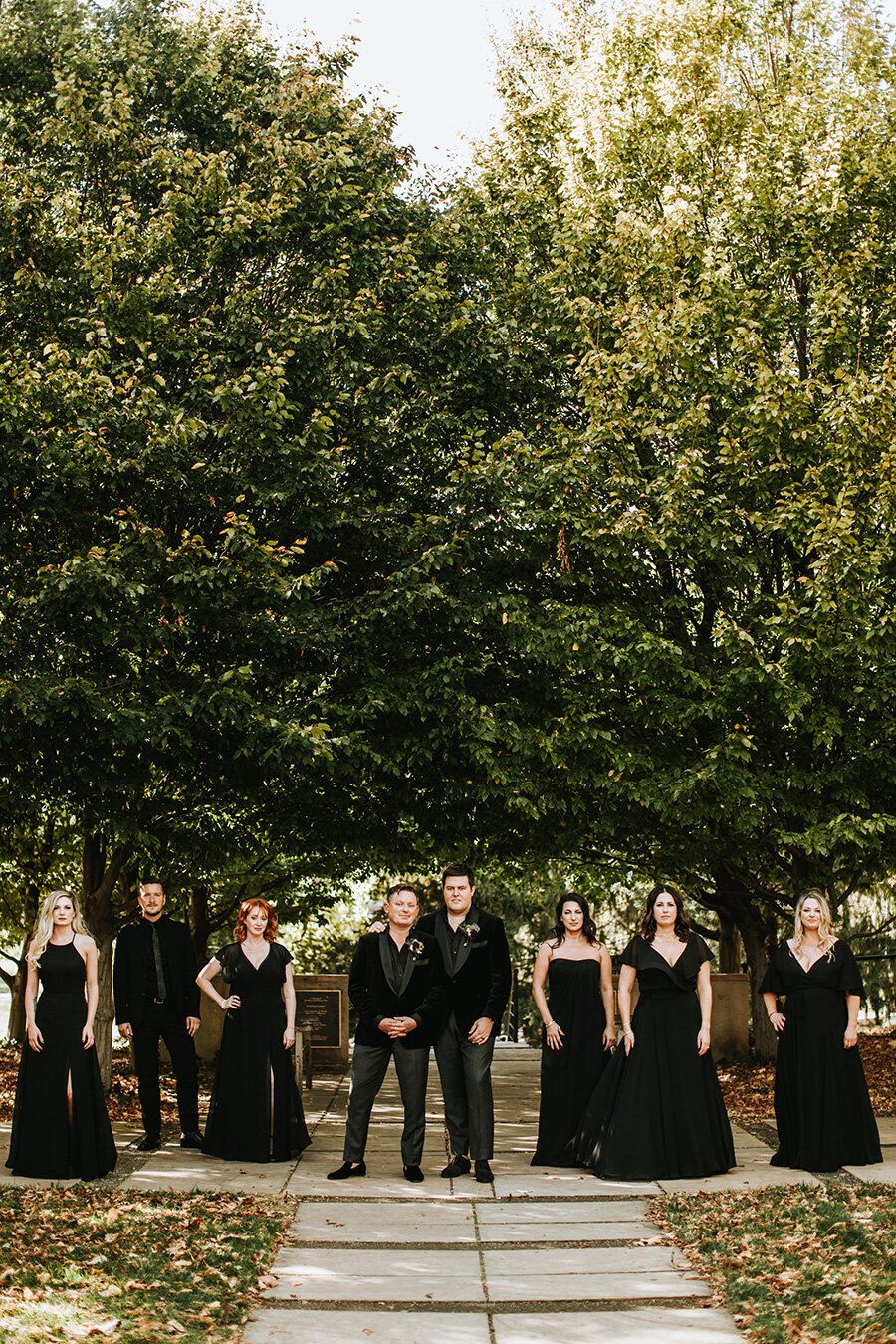 Wedding party wearing all black outdoors surrounded by large trees.